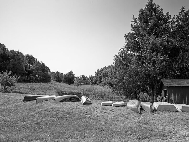 Black and white image of canoes in a row on grass